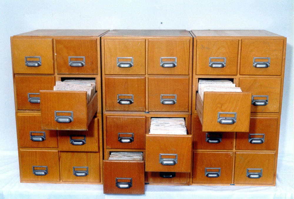 A vintage wooden Zettelkasten filing cabinet with open drawers showing handwritten index cards used for knowledge organization
